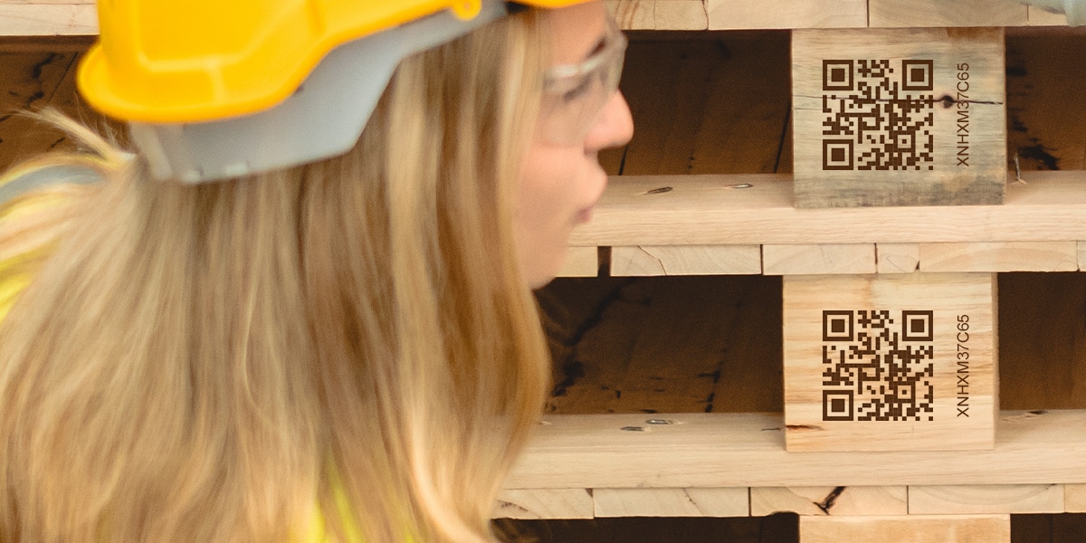 A lady with a hard hat and goggles on, inspecting QR codes on pallets.