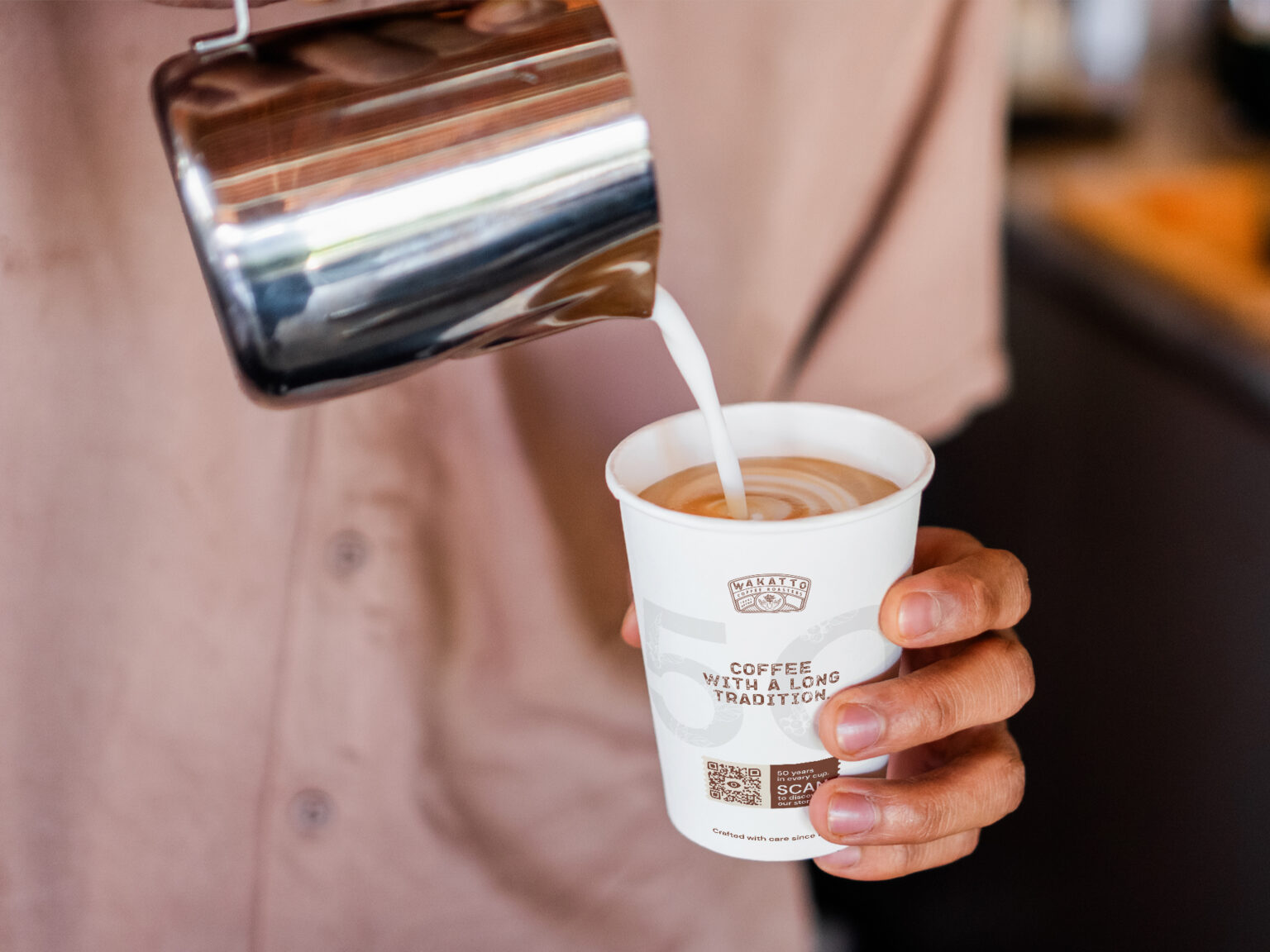someone pouring milk into a paper coffee cup that has a qr code on it