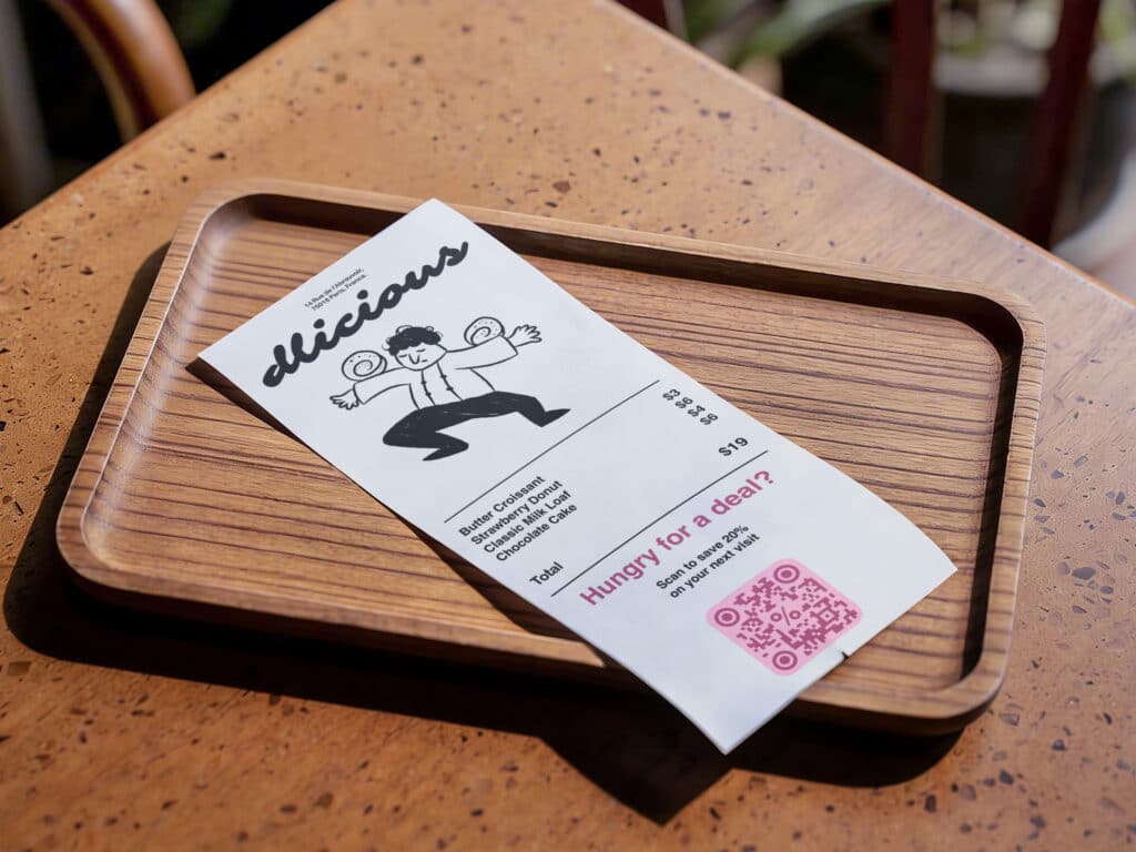 a pink qr code on a receipt laying in a wooden dish on a table